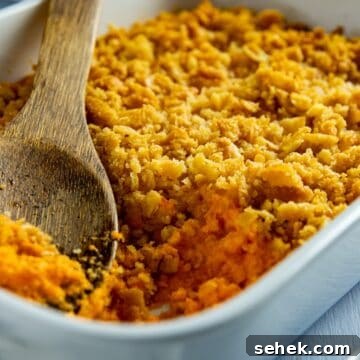 Baked carrot casserole in a white casserole dish. A wooden serving spoon is scooping out a portion.