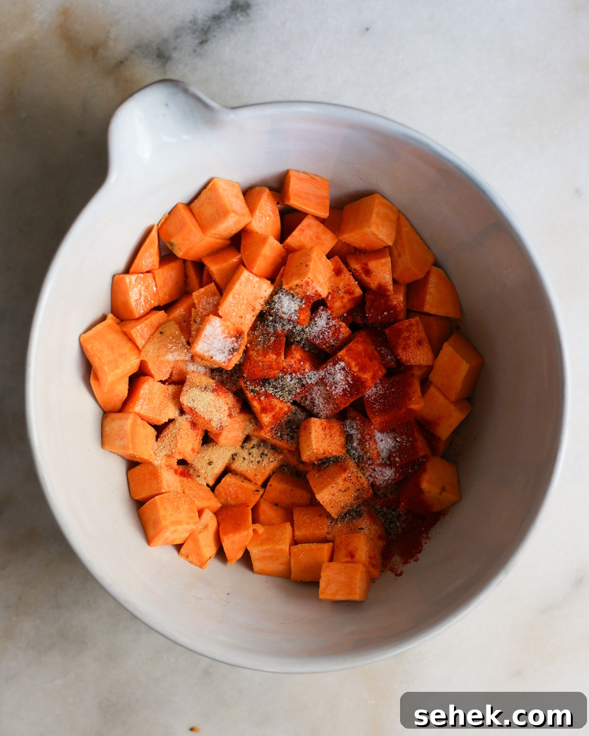 Perfectly Roasted Sweet Potatoes: Crispy Edges & Tender Centers 7 Sweet potato cubes with spices added.