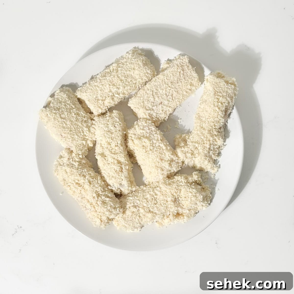 Crispy Fish Goujons Recipe — Crunchy Baked or Fried Fish Sticks 8 Raw fish goujons, crumbed on a plate.