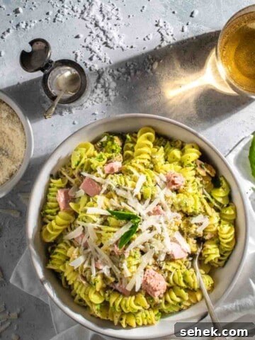 Tuna pesto pasta in a white bowl with a bowl of parmesan and a drink.