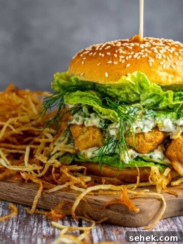An ultimate fish finger sandwich on a wooden board with a side of shoestring fries.