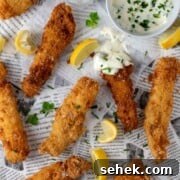 Crispy Fish Goujons Recipe — Crunchy Baked or Fried Fish Sticks 12 Fish goujons spread out on newspaper with some lemon slices and a garlic mayo dipping sauce on a small saucer.
