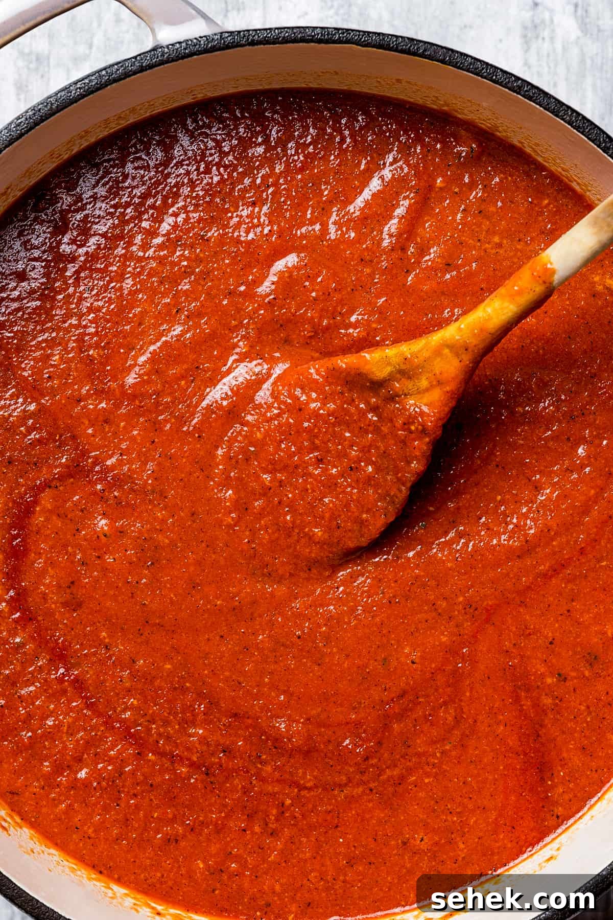 This creamy tomato bisque is delicious and so easy to make with canned tomatoes, heavy cream, and Parmesan cheese. A perfect soup for lunch or dinner. Overhead shot of tomato bisque in a soup pot, and a wooden spoon stirring through it.