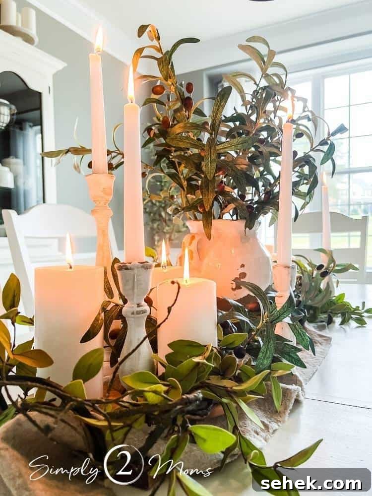 Italian-Inspired Tablescape Ideas for Elegant Dinner Parties 3 glowing candles surrounded by greenery on middle of dining table next to vase filled with olive branches