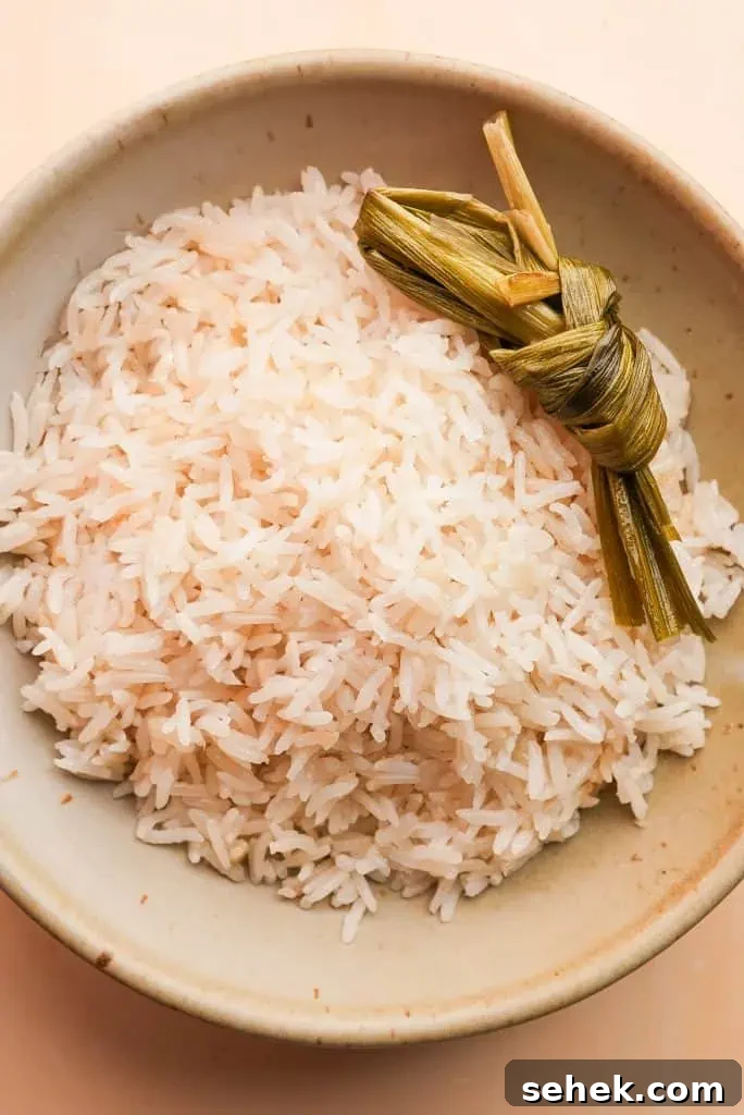 how to make coconut rice in rice cooker A bowl of freshly cooked coconut rice garnished with pandan leaves, showing light, separate grains ready to serve.