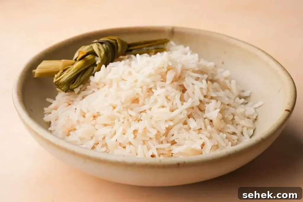 Coconut Rice Made in a Rice Cooker: Simple Fragrant Recipe 3 Close-up of cooked coconut rice in a ceramic bowl, showing long grains of jasmine rice infused with coconut milk.