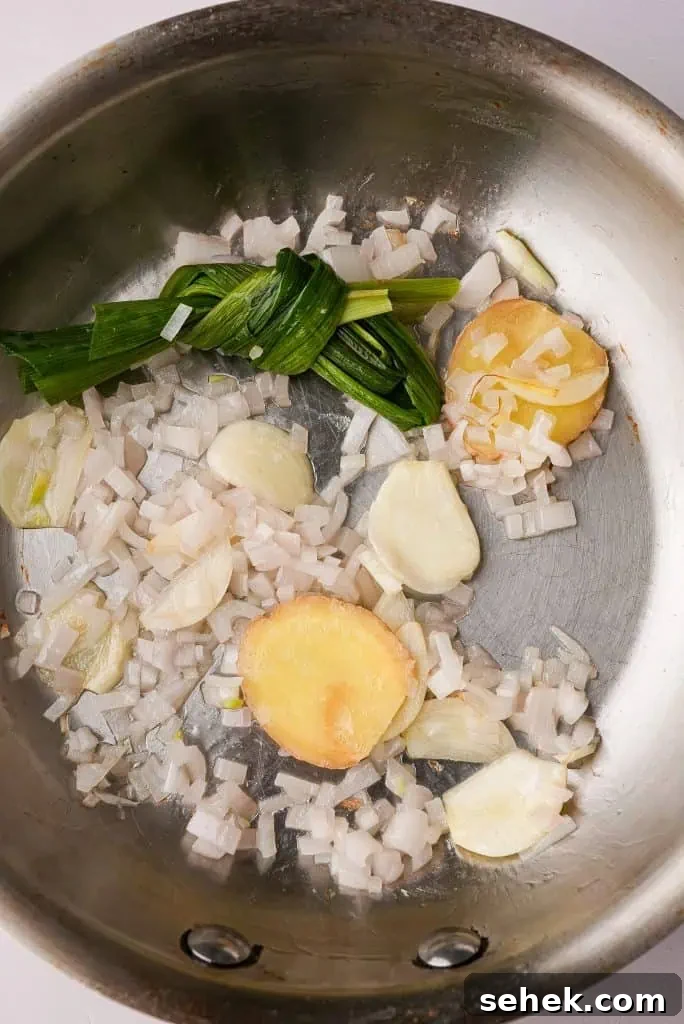 coconut rice recipe Shallots, garlic, ginger, and pandan leaves gently sautéing in a pan to build aromatic flavor for coconut rice.