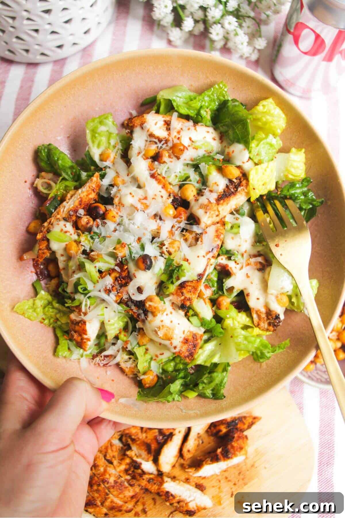 Hand holding a pink bowl filled with grilled chicken Caesar salad.