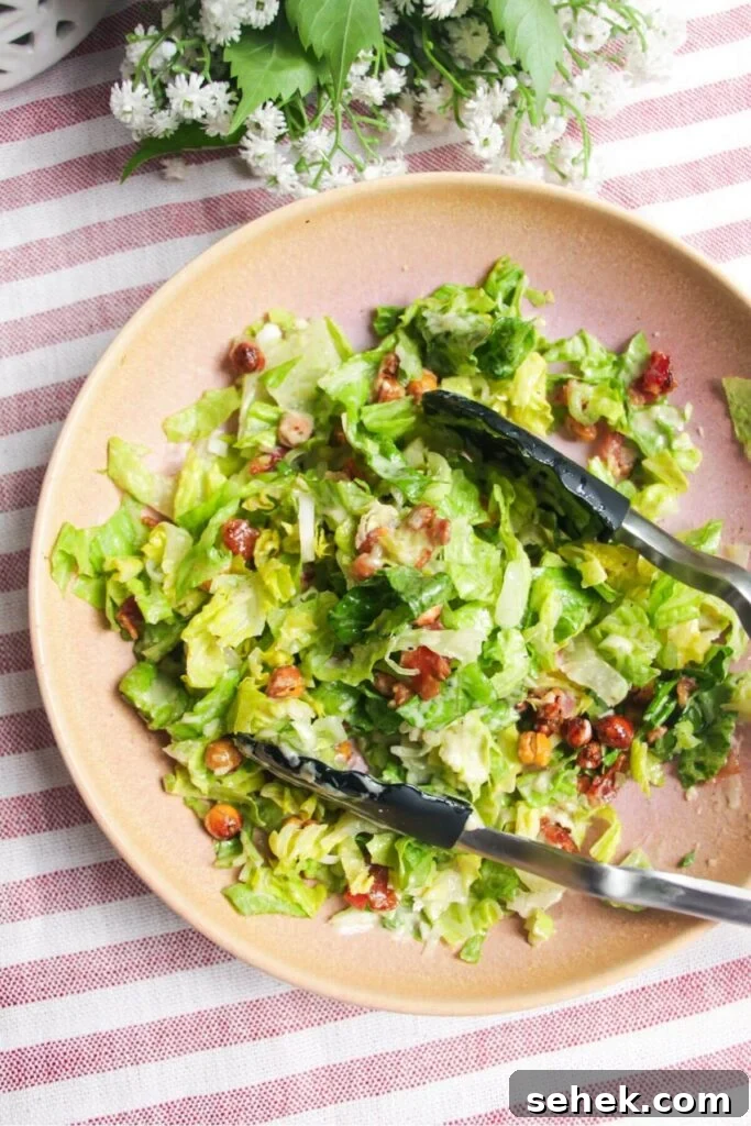 Salad mixed with tongs in a pink bowl.