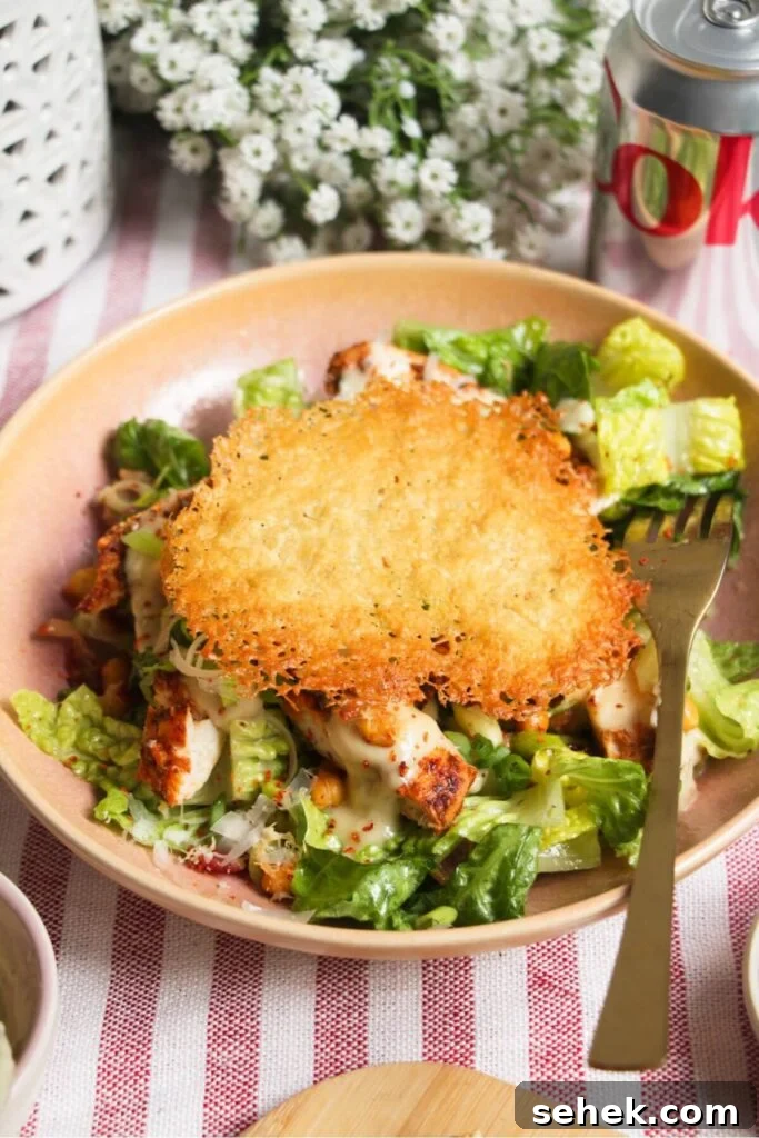 Large parmesan crisp on top of grilled chicken Caesar salad in a pink bowl.