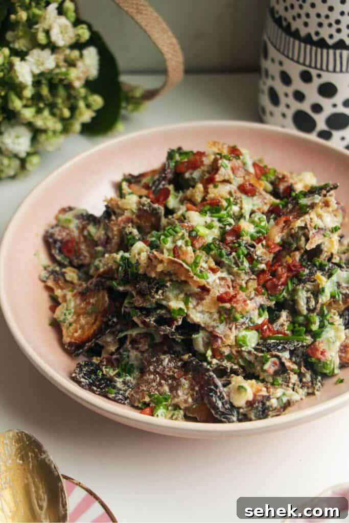Smashed potato salad in a pink bowl with chives scattered on top.