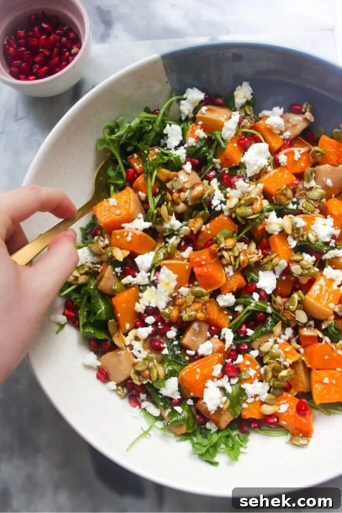 Hand holding a gold spoon, stirring colourful butternut squash salad.