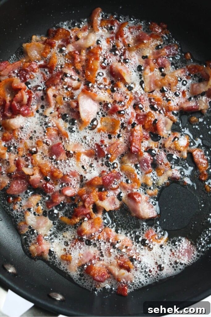 Chopped bacon cooking in a small black pan.