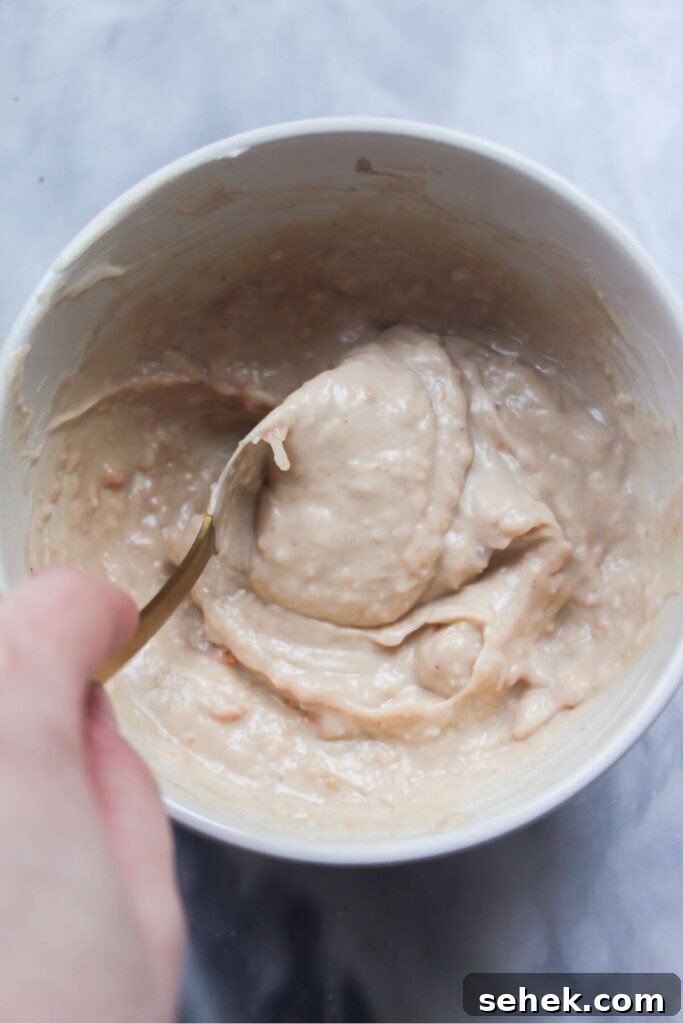 Hand mixing Caesar salad dressing in a small white bowl.