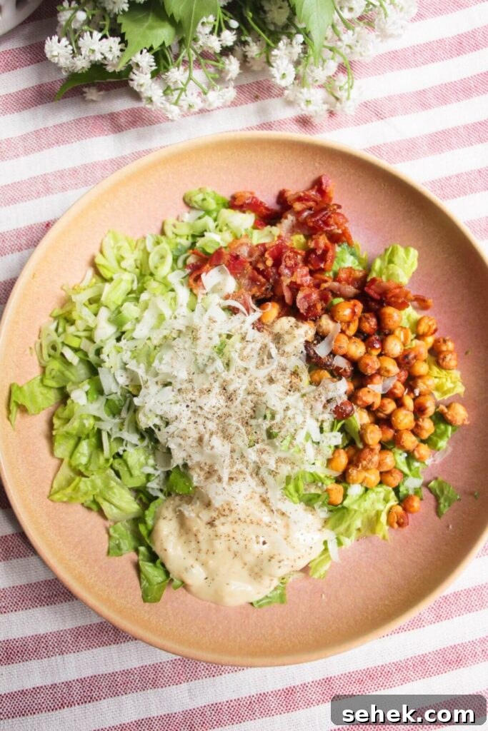 Chopped lettuce, scallions, bacon, parmesan, chickpeas and dressing in a pink bowl.
