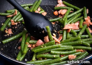Garlic Green Beans with Crispy Bacon and Lemon Zest 14 Green beans with garlic and bacon being cooked and stirred in a frying pan