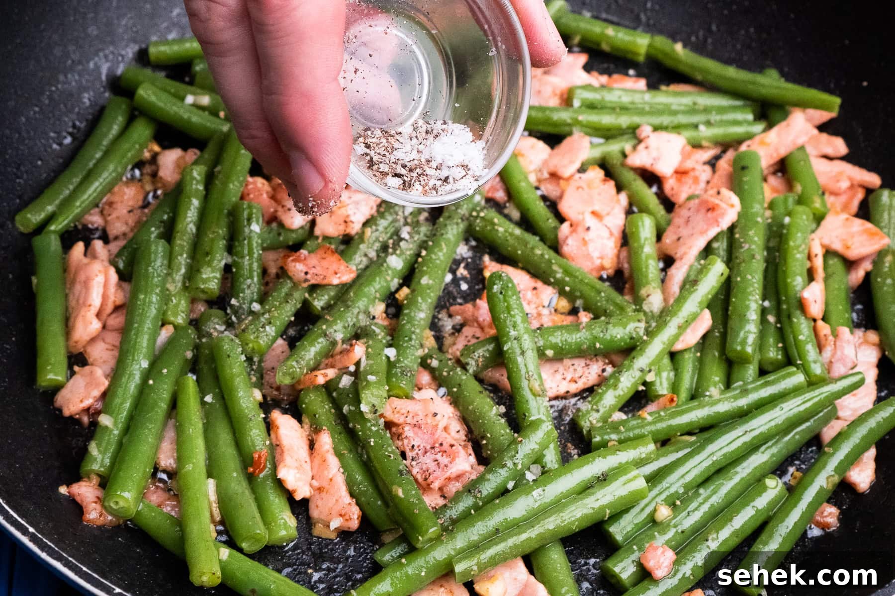 Garlic Green Beans with Crispy Bacon and Lemon Zest 29 Salt and pepper being sprinkled on top of the green beans and bacon in a frying pan
