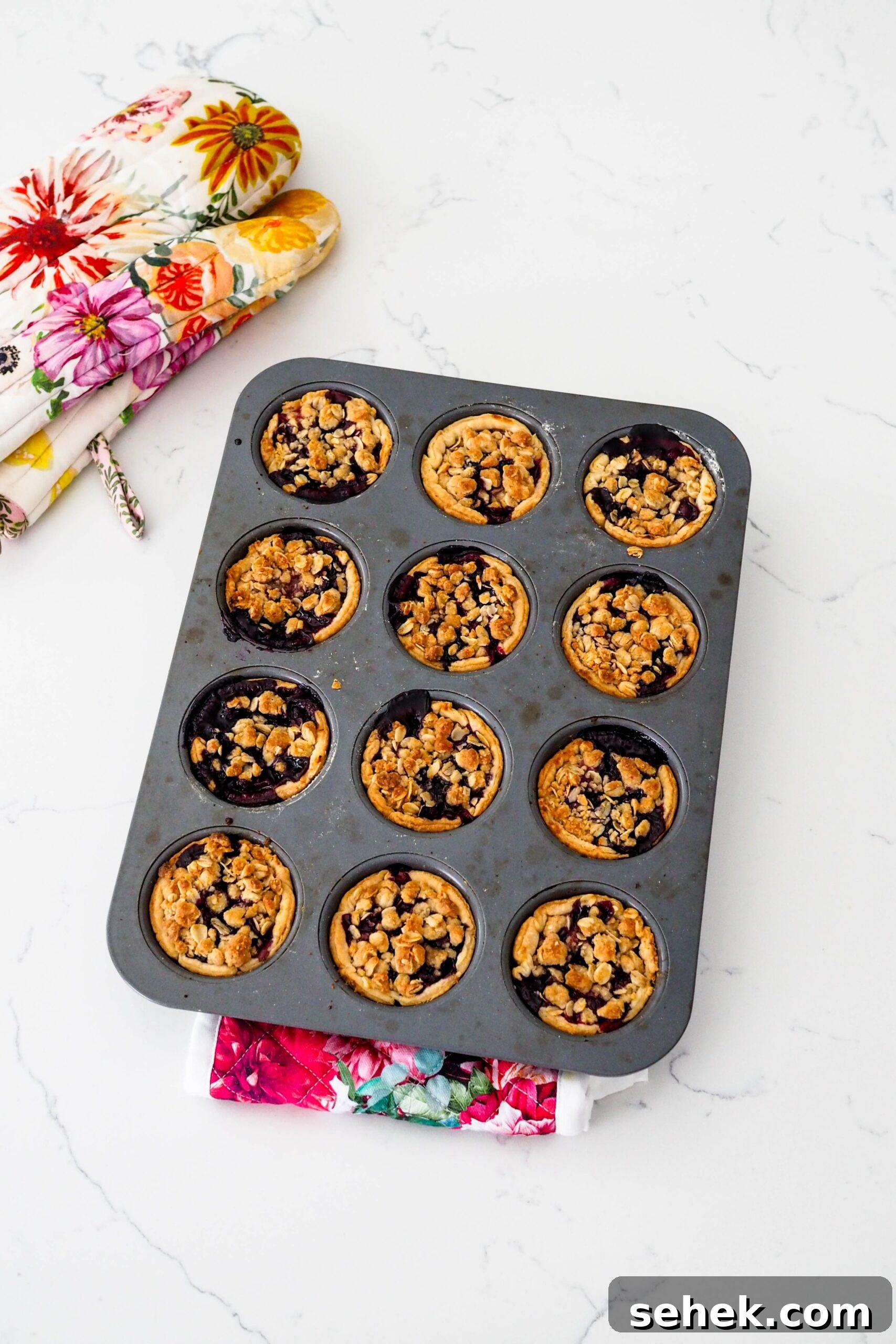 Mini Blueberry Hand Pies: Bite-Sized Fruit Desserts for Any Occasion 11 Mini blueberry pies in a muffin pan fresh out of the oven.
