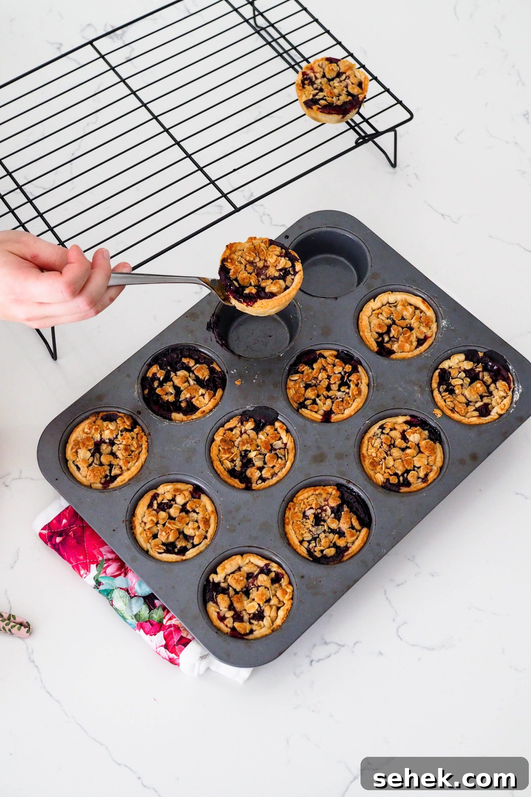 Mini Blueberry Hand Pies: Bite-Sized Fruit Desserts for Any Occasion 12 A mini pie is removed from a muffin pan with a fork and placed on a wire rack.