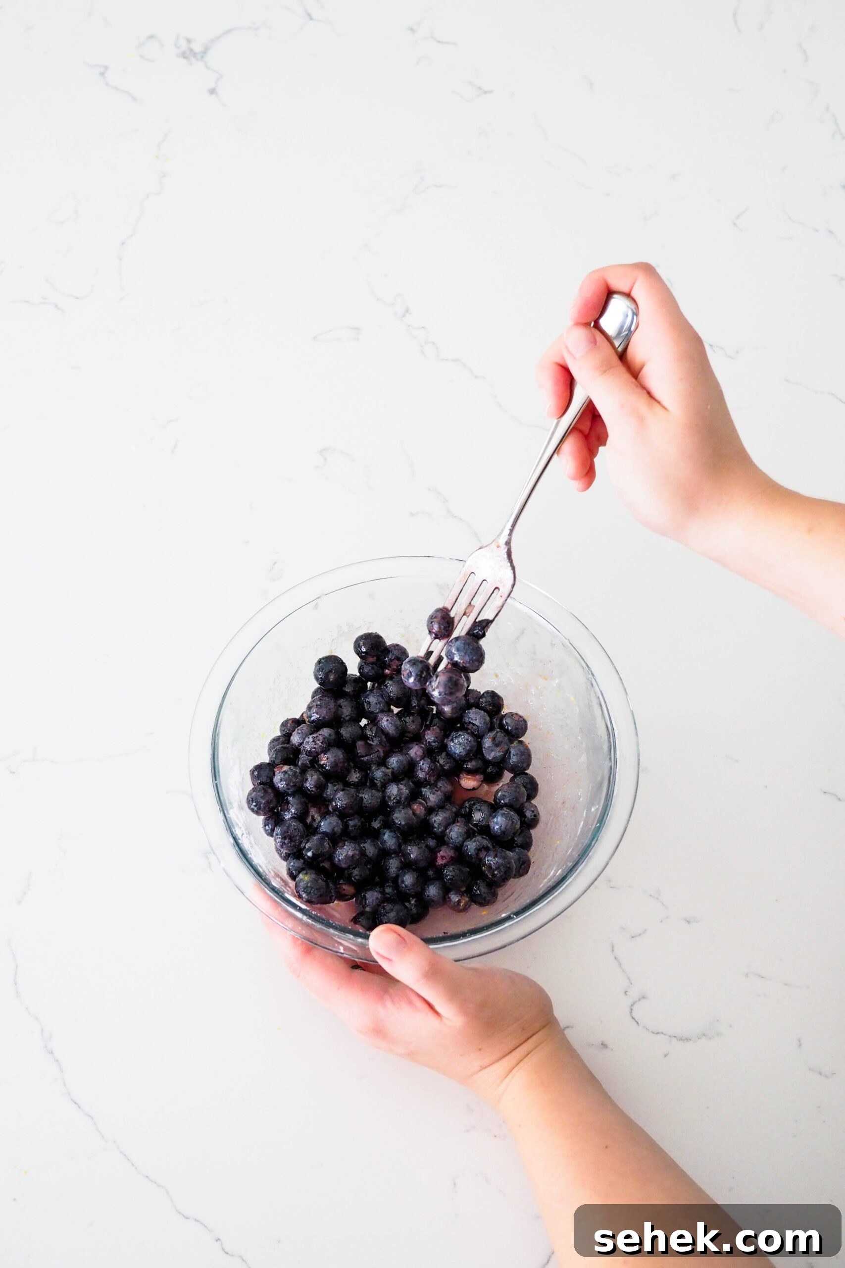 Mini Blueberry Hand Pies: Bite-Sized Fruit Desserts for Any Occasion 4 A hand pokes blueberries in a bowl with a fork.