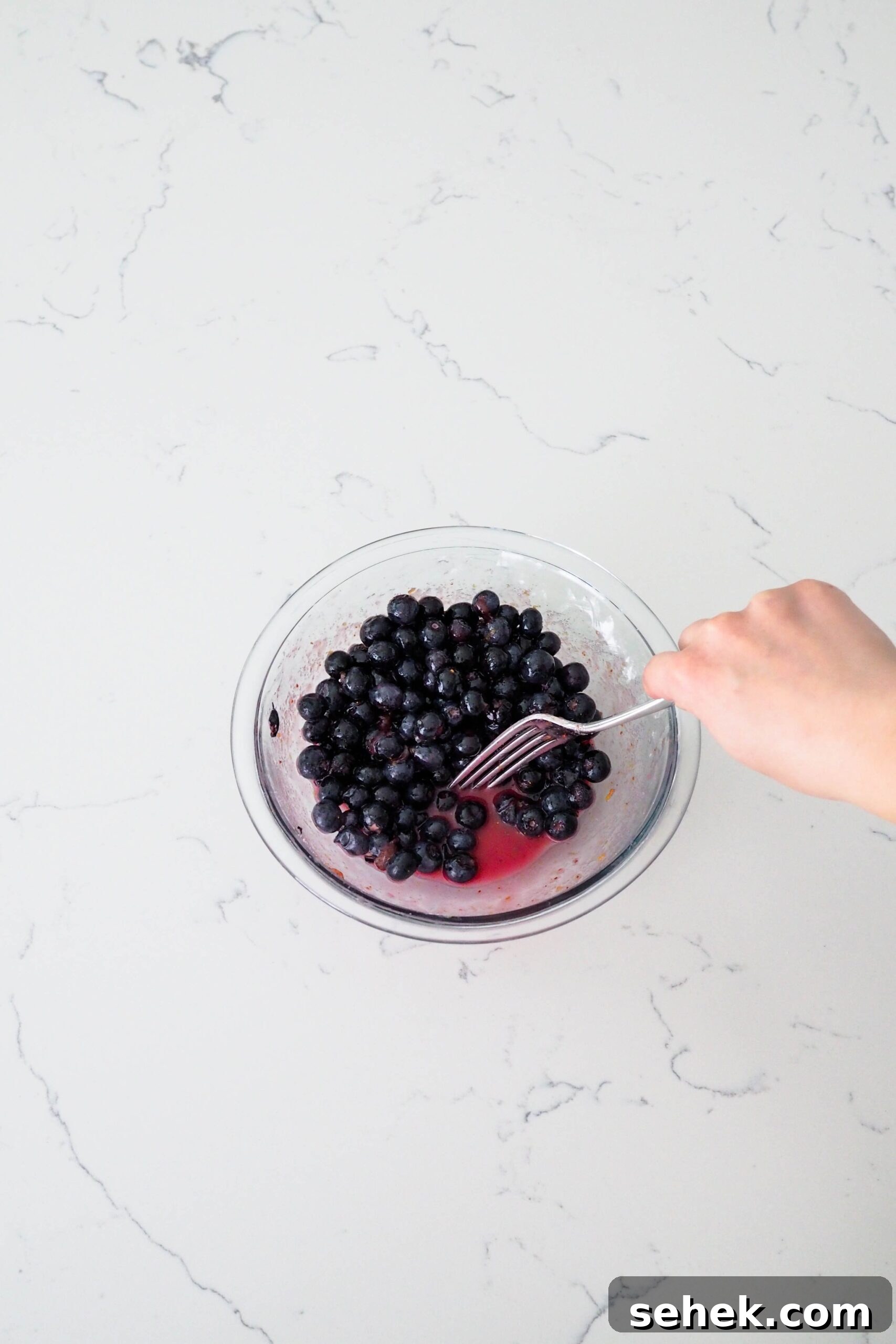 Mini Blueberry Hand Pies: Bite-Sized Fruit Desserts for Any Occasion 5 A fork pushes blueberries to the side of a bowl to show the pink liquid at the bottom.