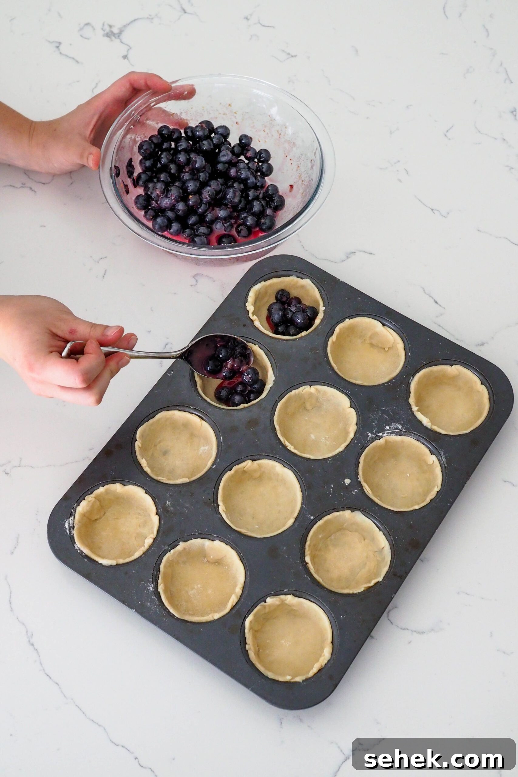 Mini Blueberry Hand Pies: Bite-Sized Fruit Desserts for Any Occasion 8 A hand spoons blueberry pie filling into mini blueberry pie shells.