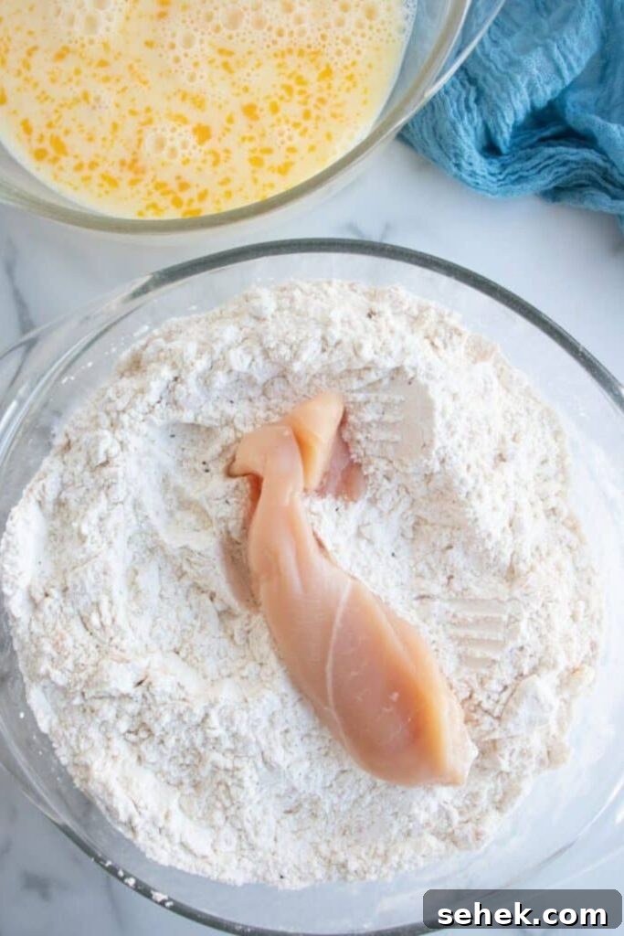 Crispy Homemade Chicken Strips: Oven-Baked & Buttermilk-Marinated 5 chicken tenderloin sitting on a flour mixture on plate