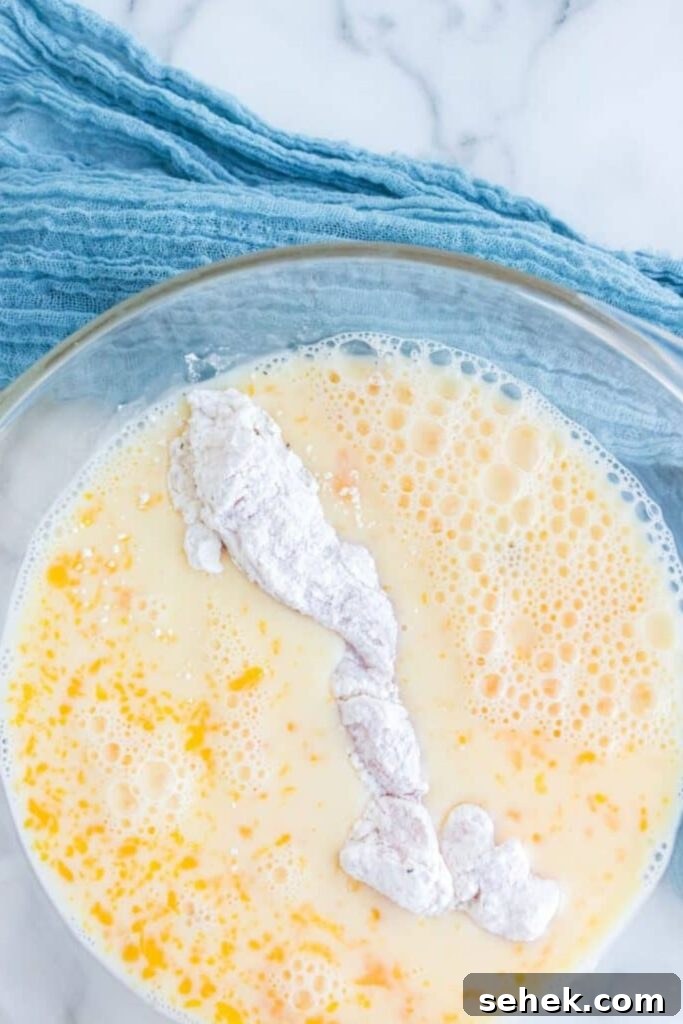 Crispy Homemade Chicken Strips: Oven-Baked & Buttermilk-Marinated 6 breaded chicken being dipped in an egg wash in a glass bowl sitting on table