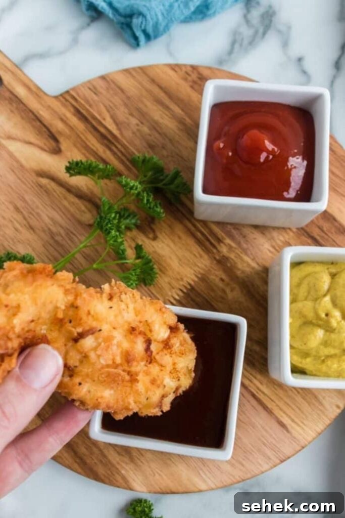 Crispy Homemade Chicken Strips: Oven-Baked & Buttermilk-Marinated 8 chicken strip being dipped in bbq sauce on table
