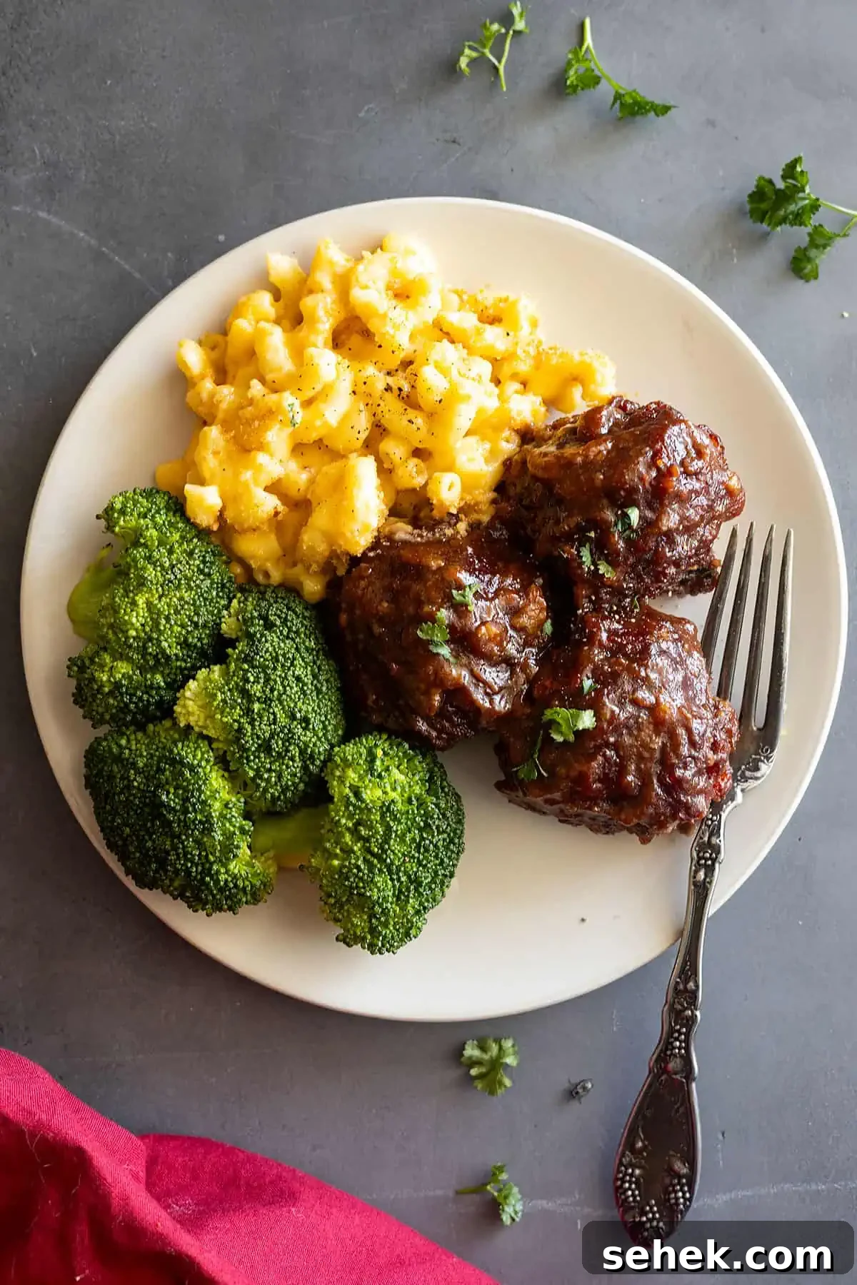 Sticky BBQ Meatballs Recipe That Melts in Your Mouth 7 overhead: BBQ meatballs on a cream plate with a fork off to the side. Red napkin in the corner