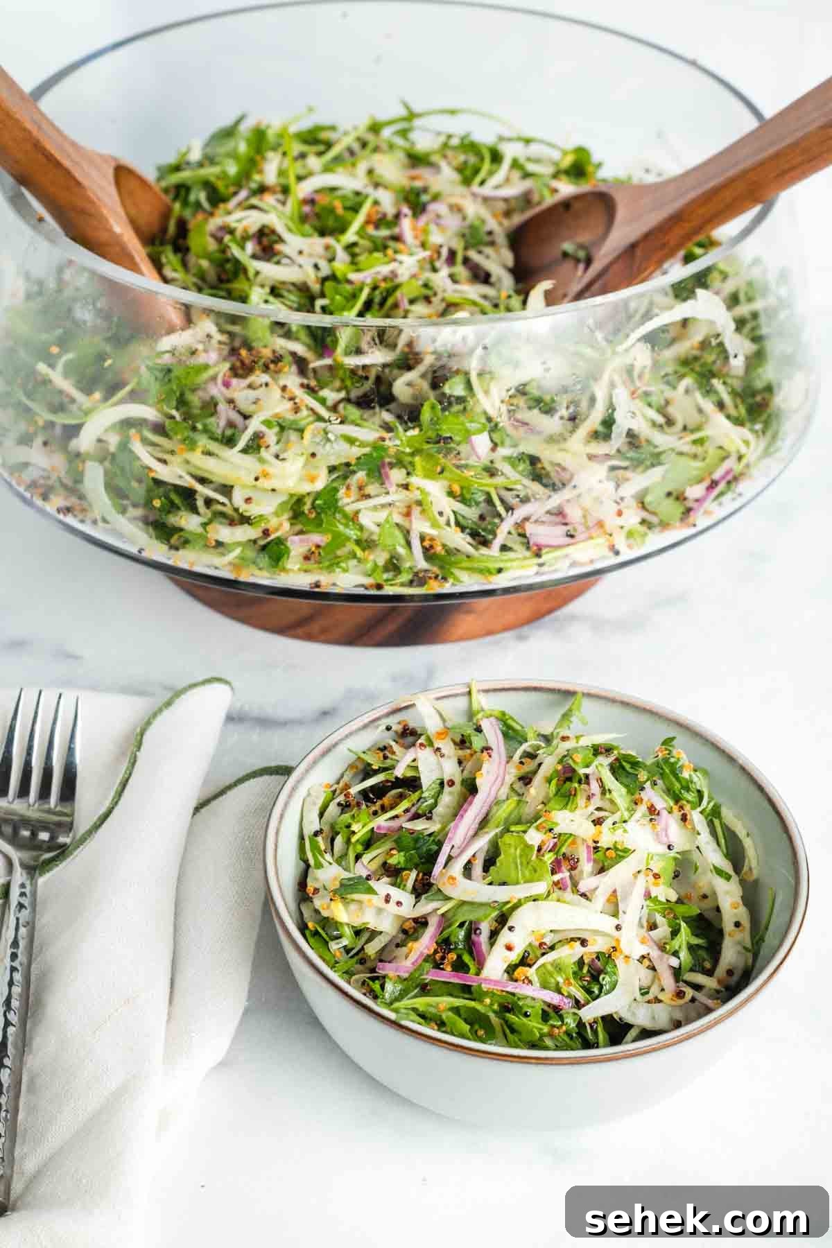 Shaved Fennel & Arugula Salad with Crispy Quinoa Crunch 2 Scooping arugula and shaved fennel salad out of a large glass bowl and into a small one.