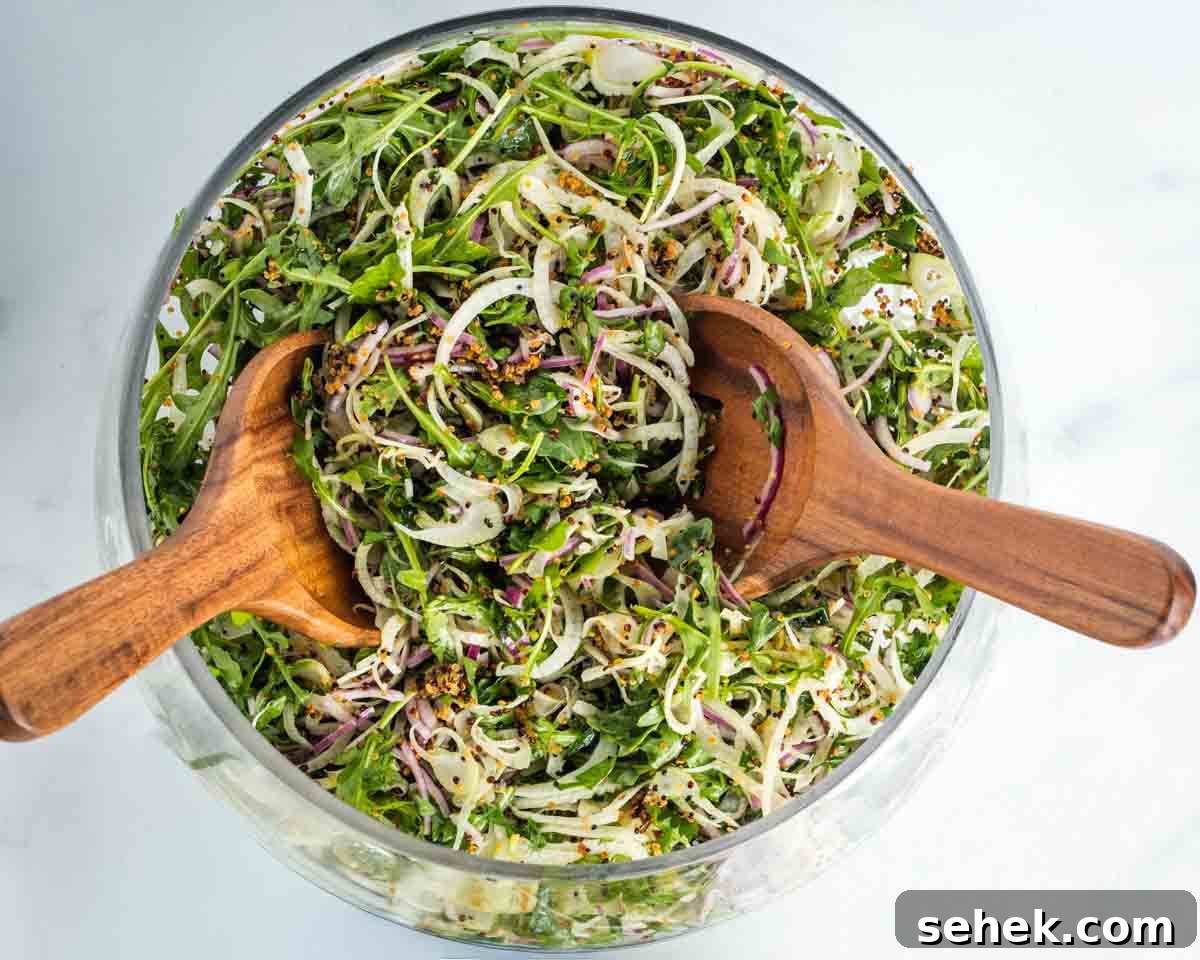Shaved Fennel & Arugula Salad with Crispy Quinoa Crunch 10 Wooden salad servers tossing a large chopped salad with greens, shaved fennel, crispy quino and red onion.