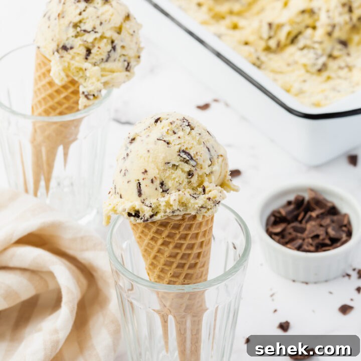 Two cones of homemade stracciatella ice cream held up in glasses, next to a white loaf pan filled with ice cream.