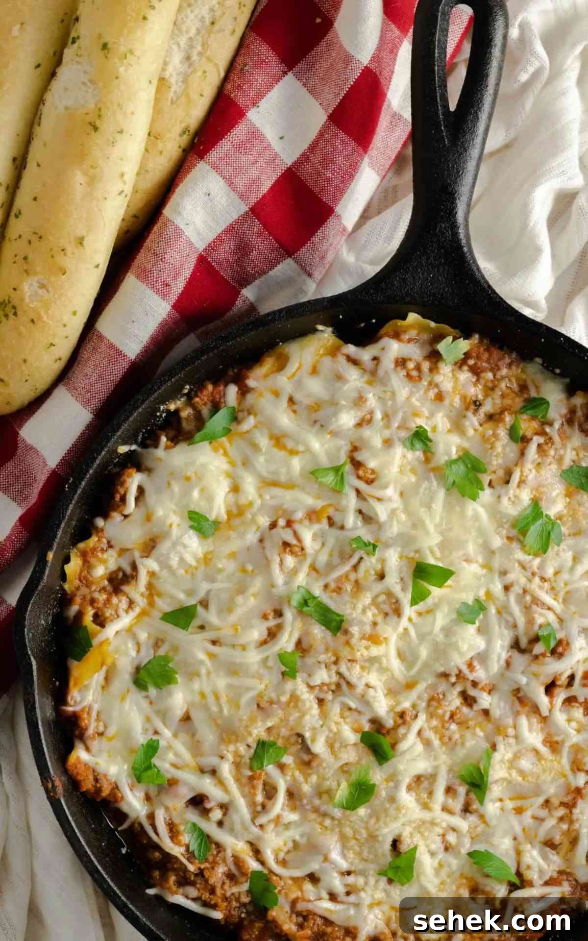 One-Pan Skillet Lasagna: Quick Weeknight Pasta Bake 2 Cast iron skillet with cheesy skillet lasagna with a side of breadsticks.