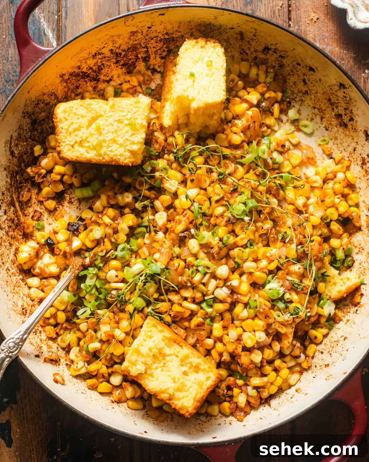 Smoky Blackened Corn with Chili-Lime Butter 2 blackened corn in a skillet with cornbread and fresh herbs on top for garnish.