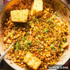 Smoky Blackened Corn with Chili-Lime Butter 7 blackened corn in a skillet with cornbread and fresh herbs on top for garnish.