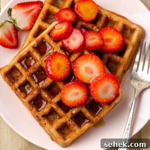 Gluten-Free Strawberry Waffle Recipe for Fluffy Breakfast 7 Two strawberry waffles topped with syrup and slices of fresh strawberries.