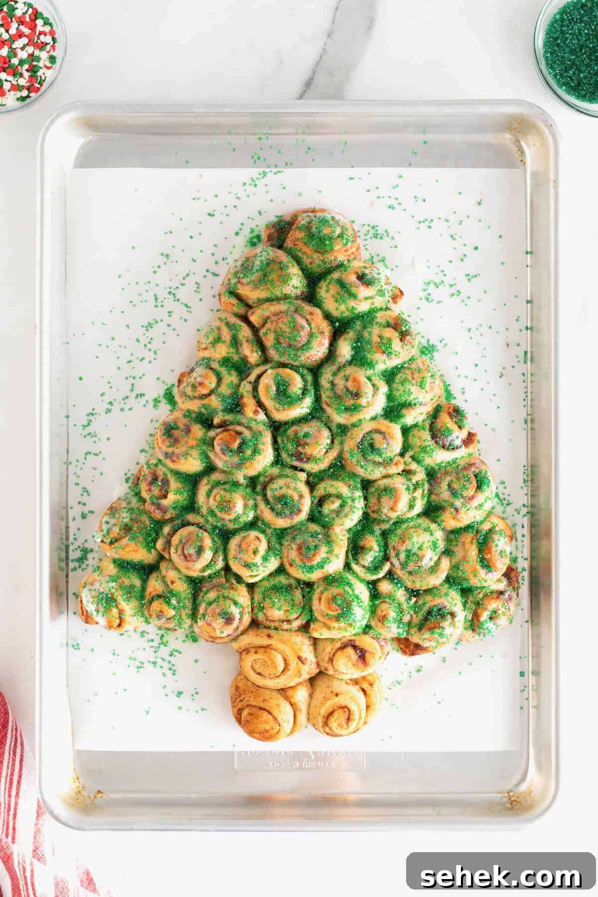 Cinnamon Roll Christmas Tree Pull-Apart Recipe 9 A cinnamon roll Christmas tree sprinkled with green sugar crystals on a parchment lined baking sheet.