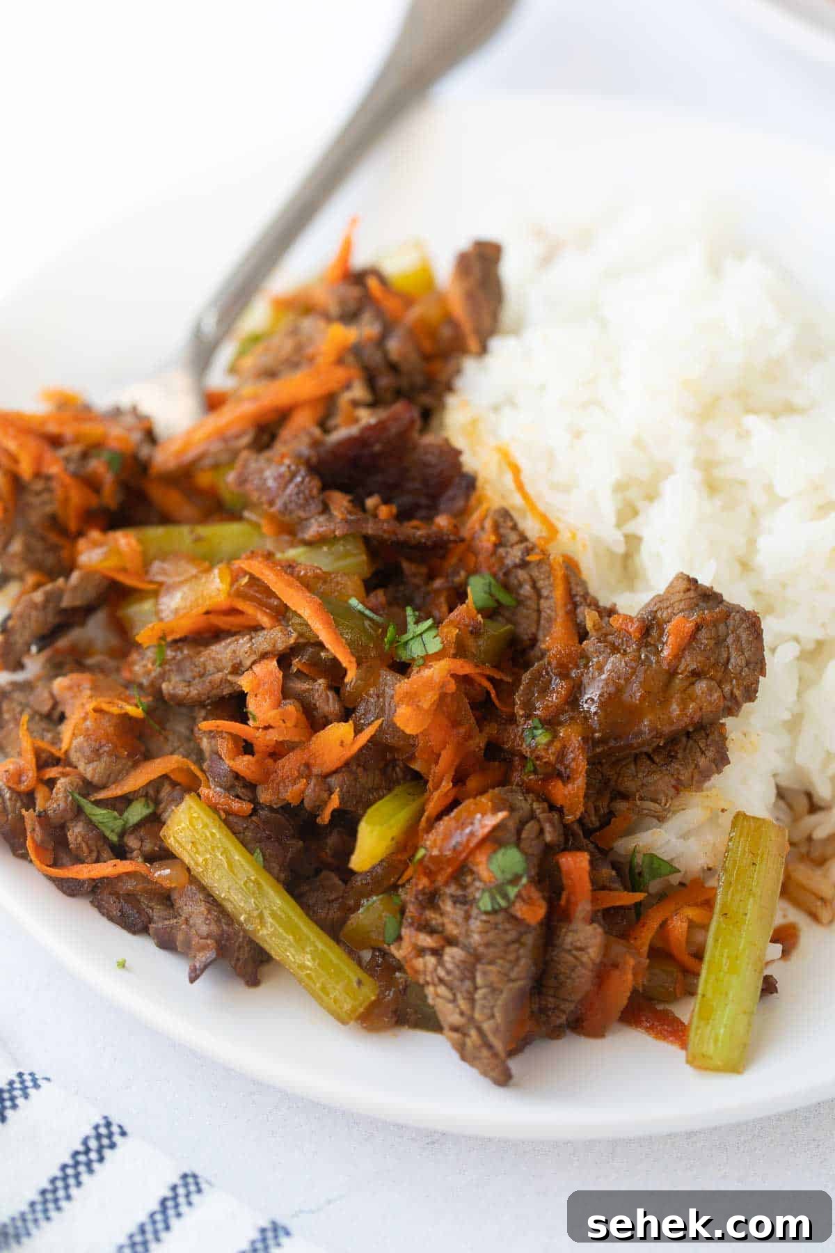 Beef Stir Fry Recipe close up of thin slices of cooked flank steak, carrots and green peppers on bed of white rice.