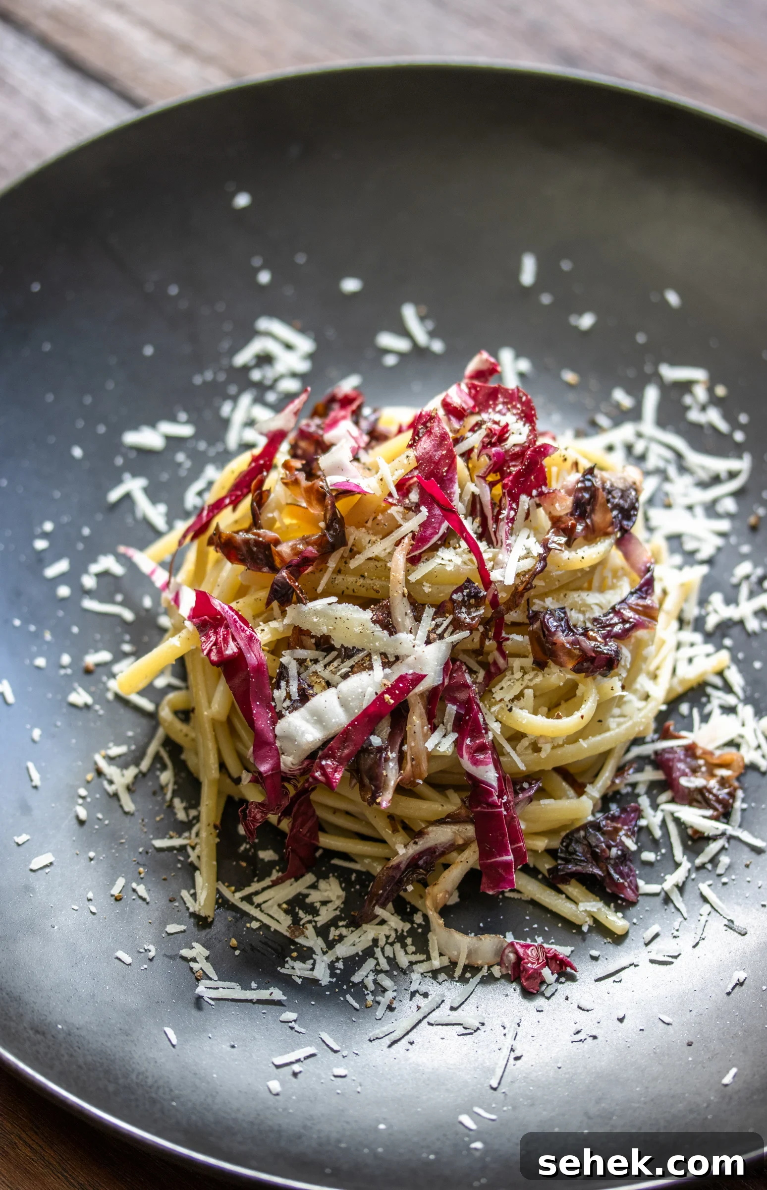 Linguine pasta, radicchio nad pecorino romano served on a black plate.