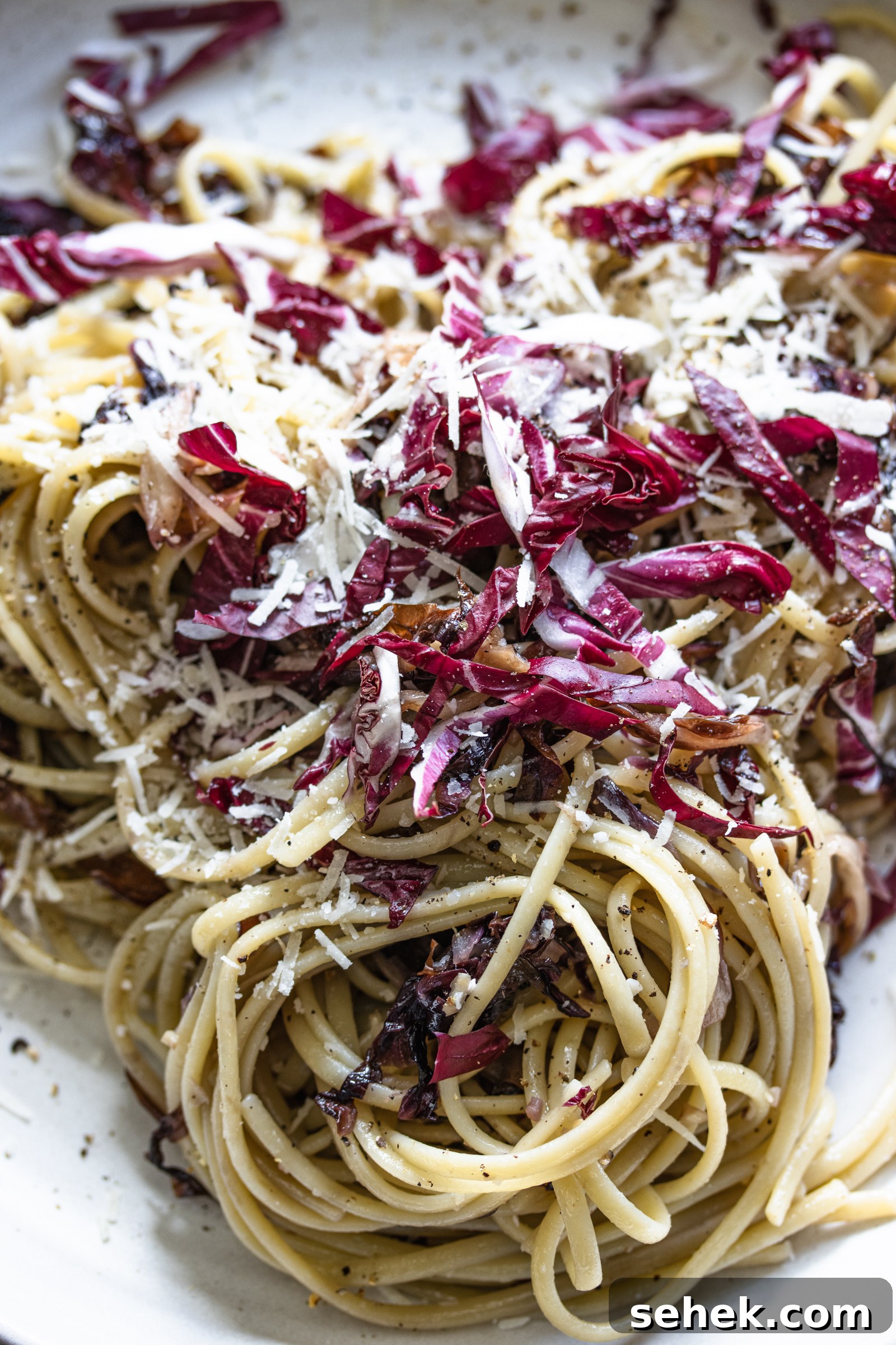 Radicchio pasta all ready and served with more grated cheese on a white plate.