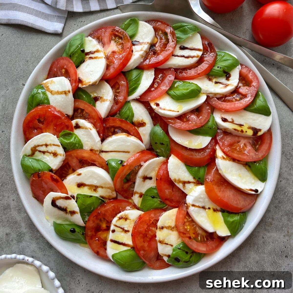 Classic Tomato Caprese Salad with Fresh Basil and Mozzarella 4 A Tomato Caprese Salad features sliced tomatoes, fresh mozzarella, basil leaves, and a drizzle of balsamic glaze, all artfully arranged in a circular pattern.