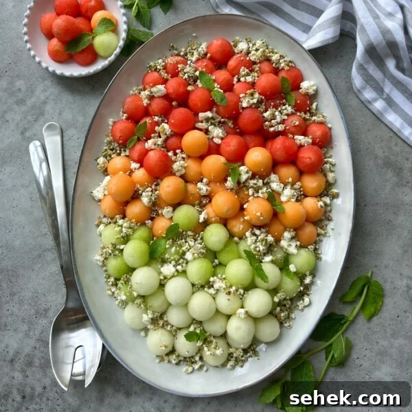 Classic Tomato Caprese Salad with Fresh Basil and Mozzarella 8 An oval platter of melon feta salad features rows of red, orange, and green melon balls topped with crumbled cheese, herbs, and seeds. Fresh mint leaves, serving utensils, a striped napkin, and a bowl of extra melon balls complete the scene.