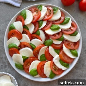 Classic Tomato Caprese Salad with Fresh Basil and Mozzarella 9 A plate of tomato caprese salad arranged in a circular pattern with alternating slices of fresh mozzarella, ripe tomatoes, and basil leaves on a gray surface.
