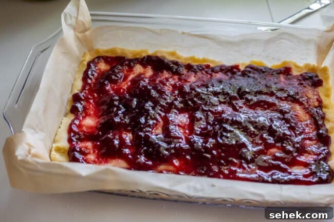 Raspberry Almond Streusel Crumble Bars 7 shortbread crust pressed into a parchment lined glass pan topped with jam.