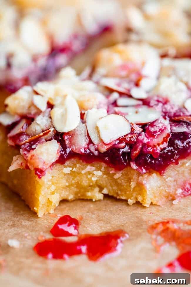 Raspberry Almond Streusel Crumble Bars 3 raspberry crumble bar on parchment paper with a bite taken out.