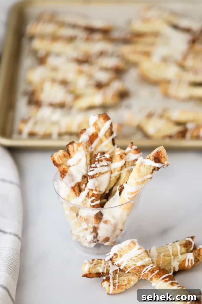 Crispy Cinnamon Puff Pastry Twists: Quick Sweet Pastry Recipe 2 A small cup full of puff pastry cinnamon twists drizzled with icing.