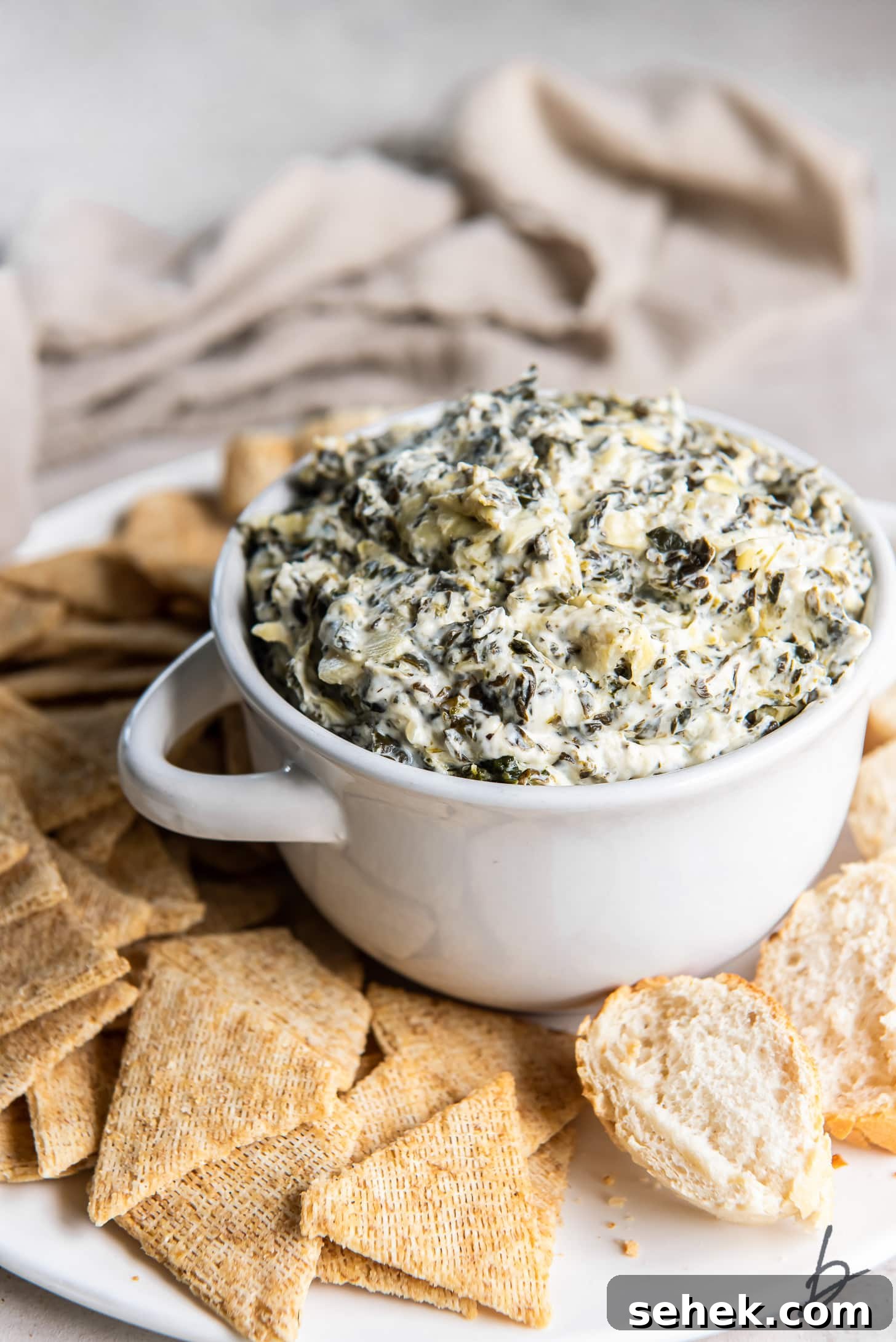 Creamy Slow Cooker Spinach Artichoke Dip Recipe 2 spinach artichoke dip in small white bowl with handles on tray with crackers