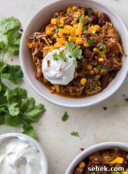 chicken chili topped with shredded cheese and sour cream in a white bowl
