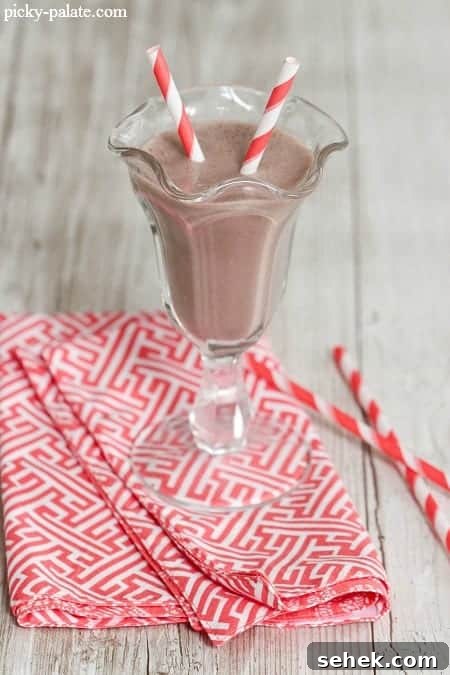 Essential Summer Drinks You Need This Season 3 A chocolate banana peanut butter smoothie in a fountain glass with two red-striped straws.